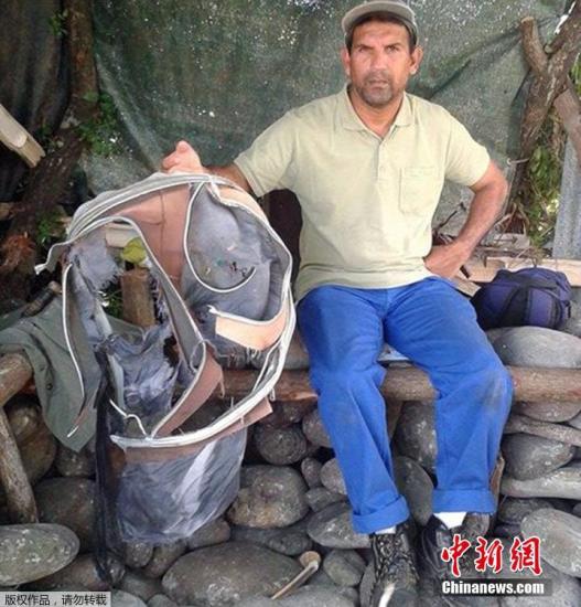 圖為當?shù)貢r間7月30日，留尼旺島上的一名海岸清潔人員展示他找到的一個手提箱的殘骸。